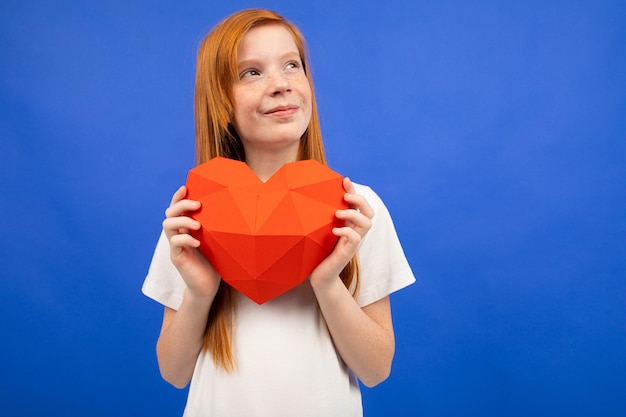 Adolescente pelirroja sosteniendo un corazón rojo hecho de papel azul con espacio de copia