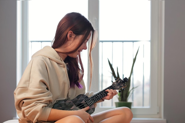 Foto adolescente con el pelo morado tocando la guitarra ukelele en su habitación