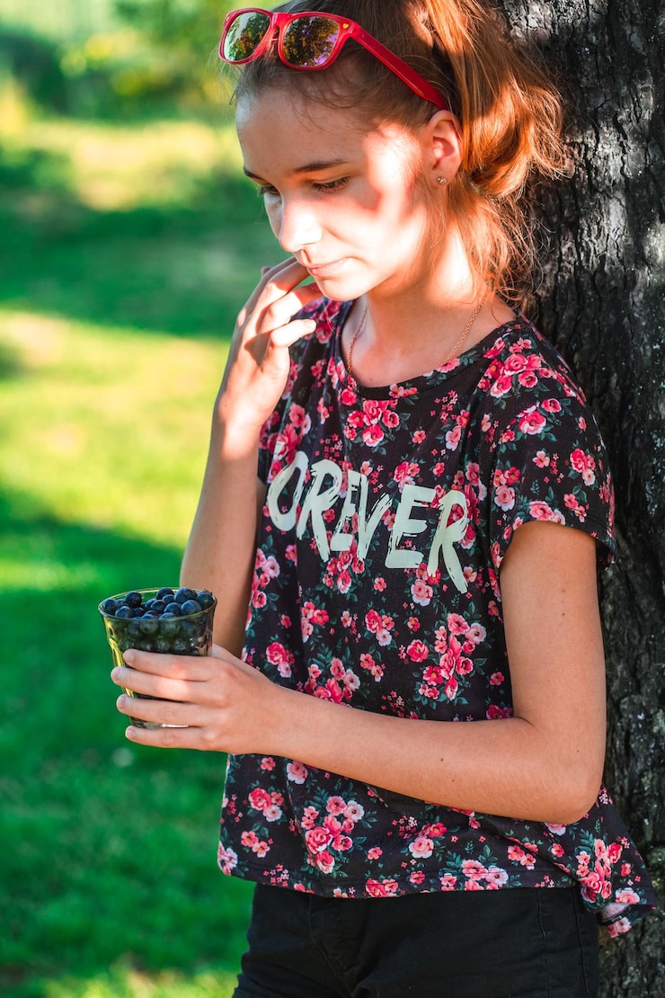 Foto adolescente pensativo sosteniendo arándanos en un vaso mientras está de pie en el jardín