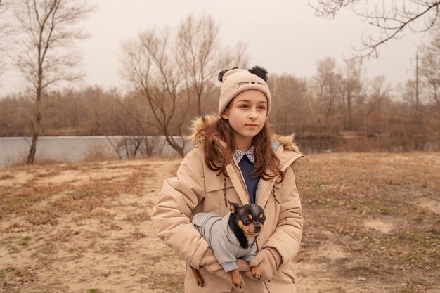 Adolescente y perro chihuahua. Niña en edad escolar y su mascota en el parque en la naturaleza. Amor por los animales.