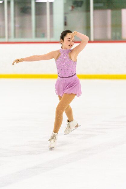 Adolescente practicando patinaje artístico en una pista de patinaje sobre hielo cubierta.