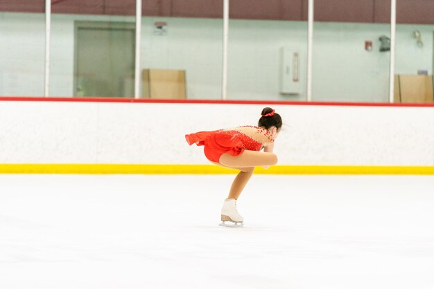 Adolescente praticando patinação artística em uma pista de patinação no gelo coberta.