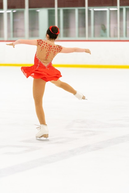 Adolescente praticando patinação artística em uma pista de patinação no gelo coberta.