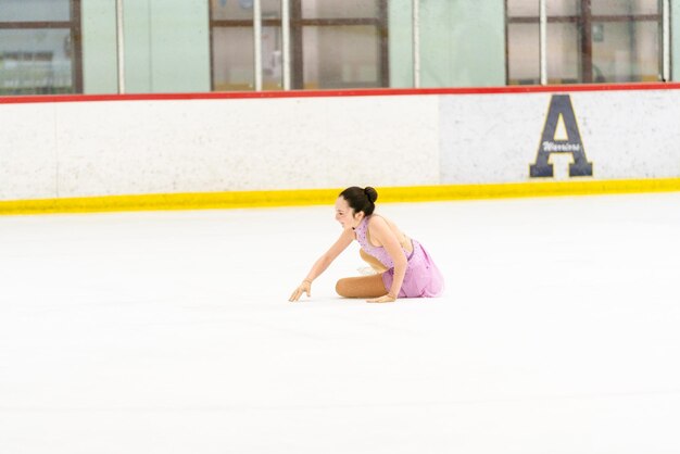Adolescente praticando patinação artística em uma pista de patinação no gelo coberta