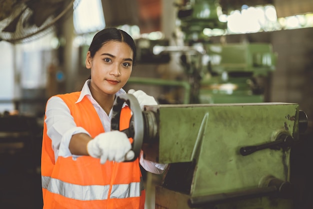 Adolescente que trabaja en la industria pesada con una sonrisa feliz en la fábrica de la industria de máquinas herramienta de torno sucio