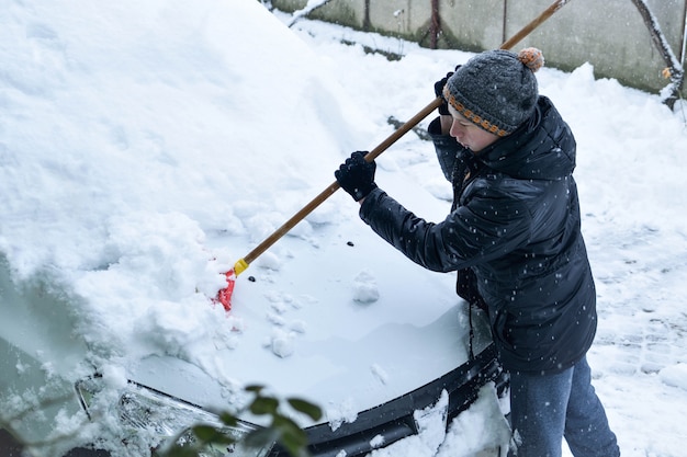 Adolescente quitando la nieve del coche con una pala en el invierno