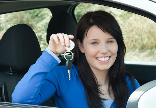 Adolescente radiante sosteniendo las llaves del coche sentado en su coche nuevo