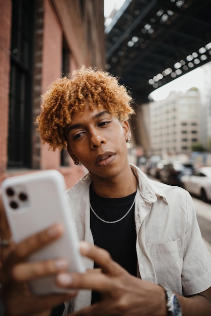 Adolescente de raza mixta activo sonriendo y escribiendo un mensaje en el teléfono inteligente mientras camina en la ciudad cu