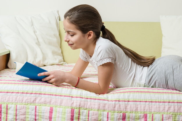 Adolescente en ropa de casa lee un libro en la cama de su habitación