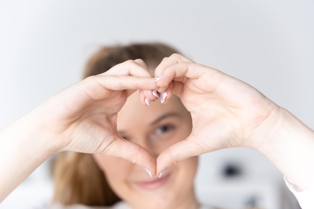 Adolescente rubia haciendo el amor o el signo del corazón con las manos