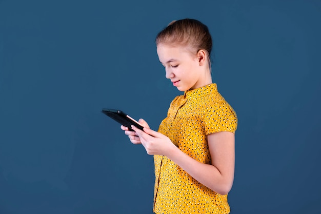 Foto adolescente rubia que juega con la tableta en la pared azul. concepto de educación
