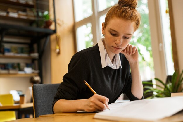 Adolescente ruiva a estudar à mesa