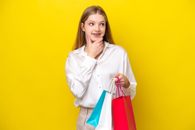 Adolescente rusa aislada de fondo amarillo sosteniendo bolsas de compras y pensando