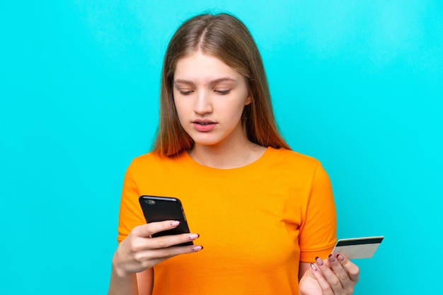 Adolescente rusa aislada de fondo azul comprando con el móvil con tarjeta de crédito