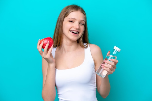 Adolescente rusa aislada de fondo azul con una manzana y una botella de agua