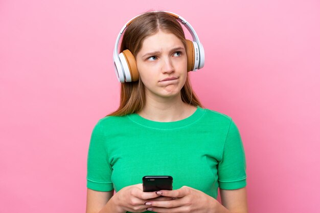 Adolescente rusa aislada de fondo rosa escuchando música con un móvil y pensando