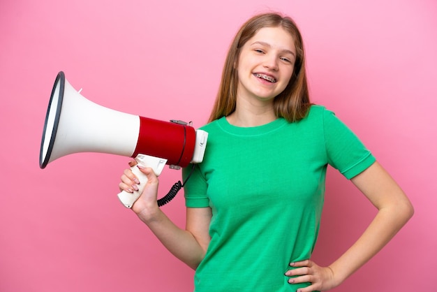 Adolescente rusa aislada de fondo rosa sosteniendo un megáfono y sonriendo