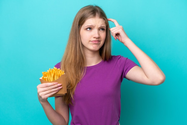 Adolescente rusa atrapando papas fritas aislada de fondo azul con dudas y con expresión facial confusa