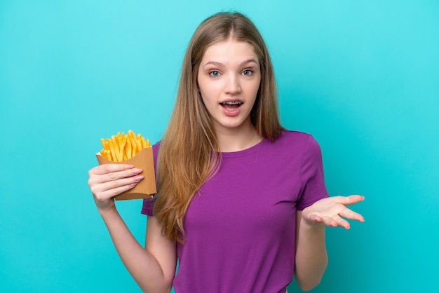 Adolescente rusa atrapando papas fritas aisladas de fondo azul con una expresión facial sorprendida