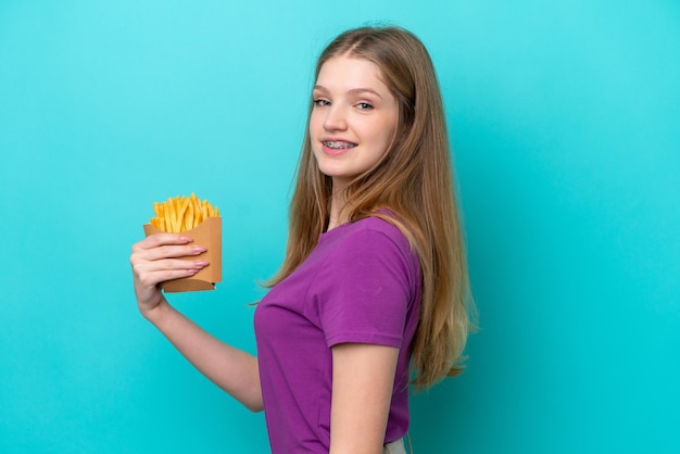 Adolescente rusa atrapando papas fritas aisladas de fondo azul sonriendo mucho