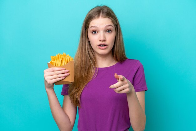 Adolescente rusa atrapando papas fritas aisladas de fondo azul sorprendida y apuntando al frente