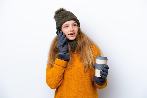 Adolescente rusa con chaqueta de invierno aislada de fondo blanco sosteniendo café para llevar y un móvil