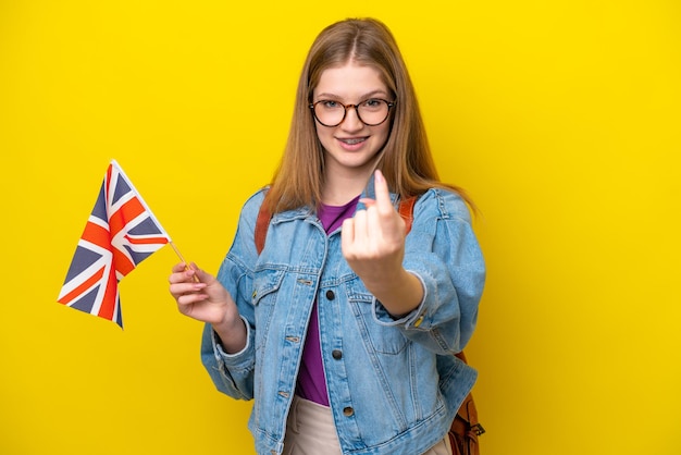 Adolescente rusa sosteniendo una bandera del Reino Unido aislada en un fondo amarillo haciendo el gesto de venir