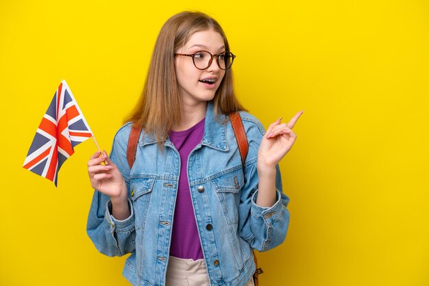 Adolescente rusa sosteniendo una bandera del Reino Unido aislada en un fondo amarillo con la intención de darse cuenta de la solución mientras levanta un dedo