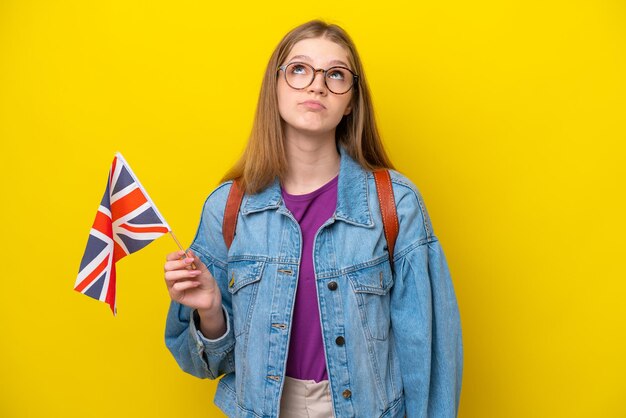 Adolescente rusa sosteniendo una bandera del Reino Unido aislada de fondo amarillo y mirando hacia arriba