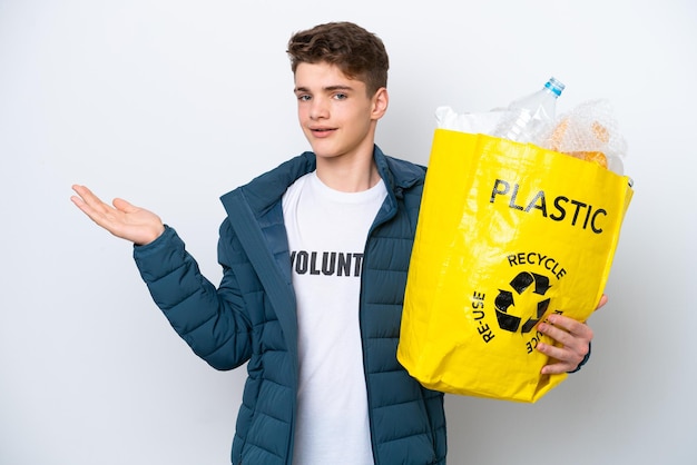 Adolescente rusa sosteniendo una bolsa llena de botellas de plástico para reciclar sobre fondo blanco extendiendo las manos a un lado para invitar a venir