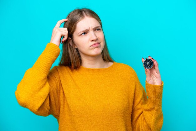 Adolescente rusa sosteniendo una brújula aislada de fondo azul con dudas y con una expresión facial confusa