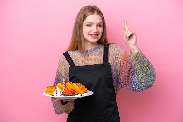 Adolescente rusa sosteniendo gofres aislados de fondo rosa señalando una gran idea