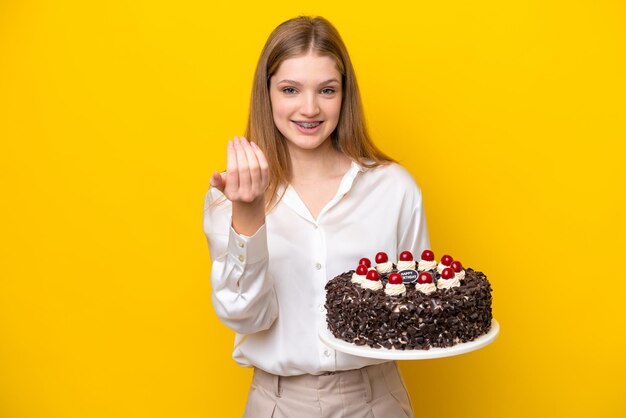 Adolescente rusa sosteniendo pastel de cumpleaños aislado de fondo amarillo invitando a venir con la mano Feliz de que hayas venido
