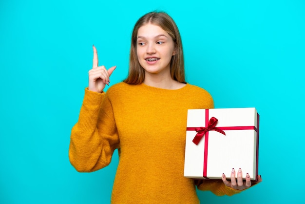 Adolescente rusa sosteniendo un regalo aislado de fondo azul con la intención de darse cuenta de la solución mientras levanta un dedo