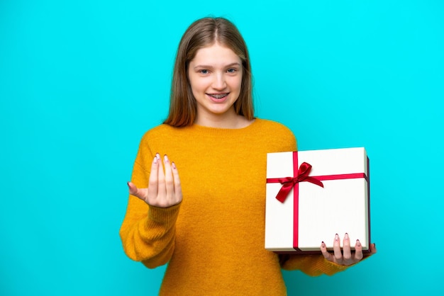 Adolescente rusa sosteniendo un regalo aislado de fondo azul invitando a venir con la mano Feliz de que hayas venido