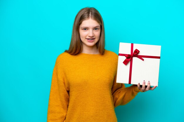 Adolescente rusa sosteniendo un regalo aislado de fondo azul sonriendo mucho