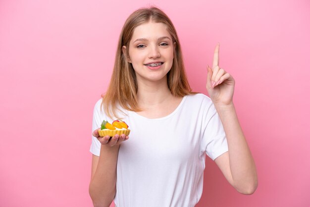 Adolescente rusa sosteniendo una tartaleta aislada de fondo rosa señalando una gran idea