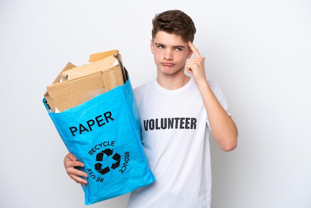 Adolescente ruso hombre sosteniendo una bolsa de reciclaje llena de papel para reciclar aislado sobre fondo blanco con dudas y pensamiento