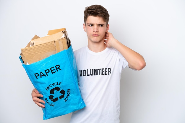 Adolescente ruso hombre sosteniendo una bolsa de reciclaje llena de papel para reciclar aislado sobre fondo blanco con dudas