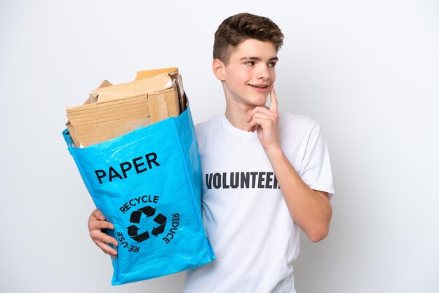 Adolescente ruso hombre sosteniendo una bolsa de reciclaje llena de papel para reciclar aislado sobre fondo blanco pensando en una idea mientras mira hacia arriba