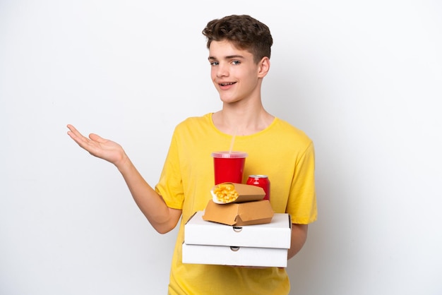 Adolescente ruso hombre sosteniendo comida rápida aislado sobre fondo blanco extendiendo las manos a un lado para invitar a venir