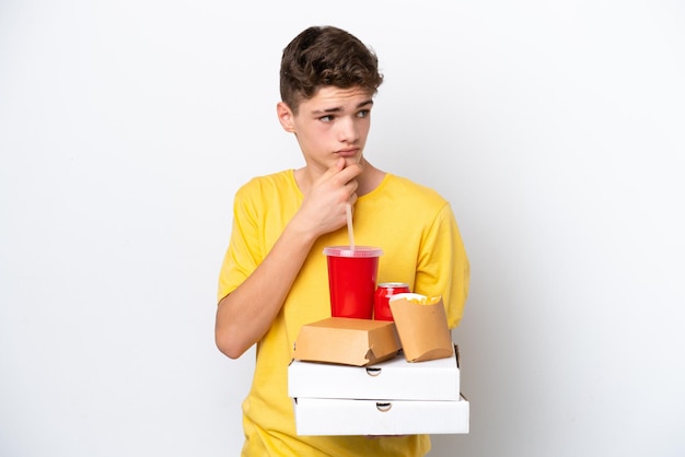 Adolescente ruso hombre sosteniendo comida rápida aislado sobre fondo blanco mirando hacia el lado y sonriendo