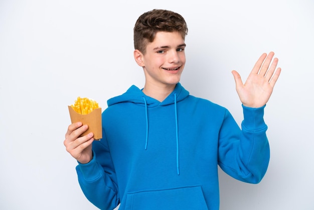 Adolescente ruso hombre sosteniendo patatas fritas aislado sobre fondo blanco saludando con la mano con expresión feliz