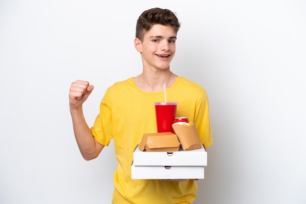 Adolescente ruso hombre sujetando comida rápida aislado sobre fondo blanco celebrando una victoria