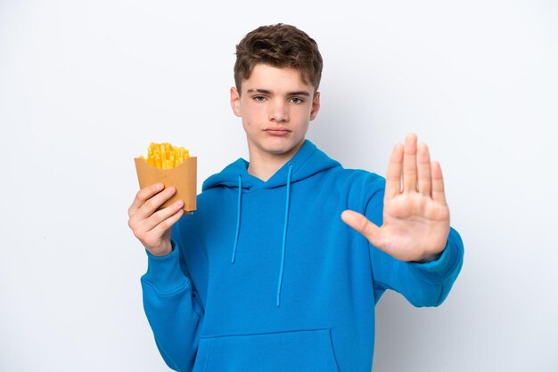 Adolescente ruso hombre sujetando patatas fritas aislado sobre fondo blanco haciendo gesto de parada