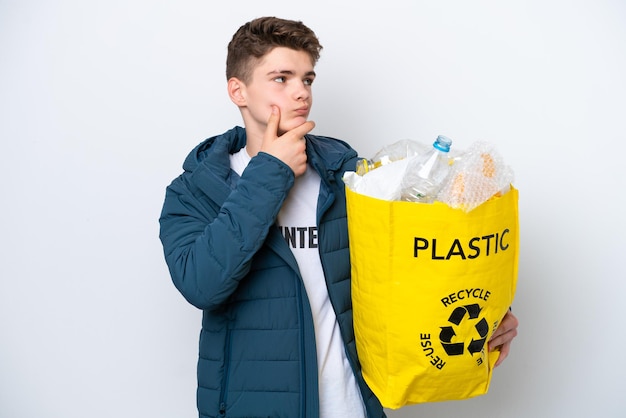 Adolescente ruso sosteniendo una bolsa llena de botellas de plástico para reciclar sobre fondo blanco con dudas