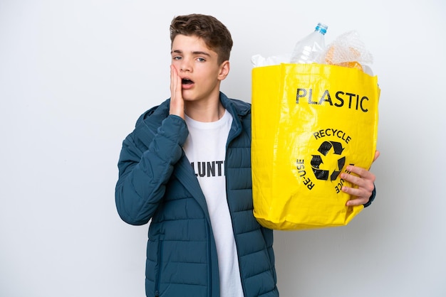 Adolescente ruso sosteniendo una bolsa llena de botellas de plástico para reciclar sobre fondo blanco con sorpresa y expresión facial conmocionada