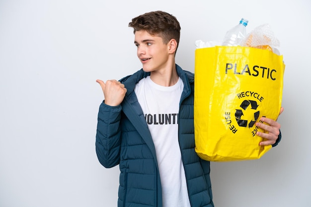 Adolescente russo segurando um saco cheio de garrafas plásticas para reciclar em fundo branco apontando para o lado para apresentar um produto