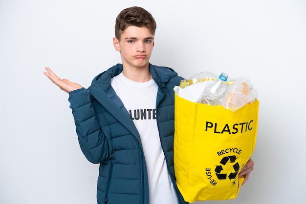 Adolescente russo segurando um saco cheio de garrafas plásticas para reciclar em fundo branco com dúvidas ao levantar as mãos