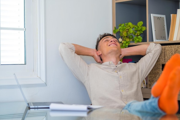 Adolescente satisfecho feliz de terminar el trabajo con la computadora portátil en casa, levanta las manos y pone los pies sobre la mesa, relajándose después de un duro día de trabajo a la espera de una licencia de fin de semana, día de trabajo relajado, sin estrés